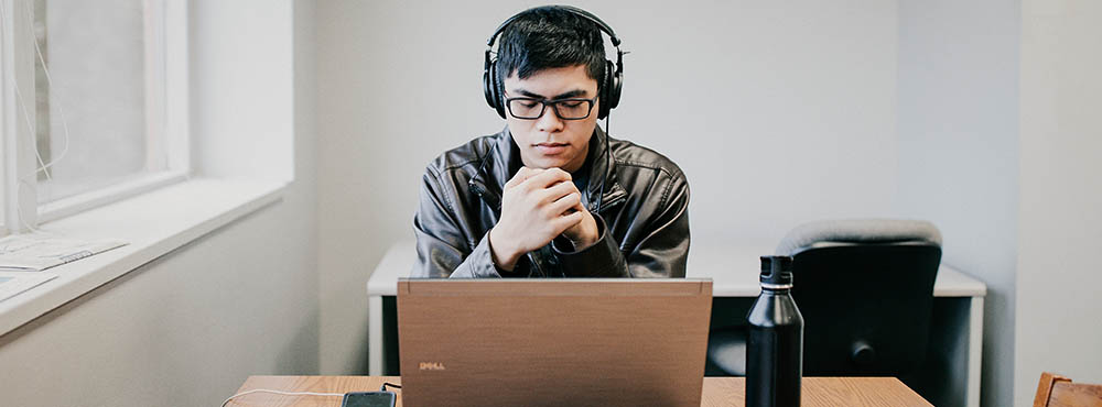 Student studying at laptop with headphones in library
