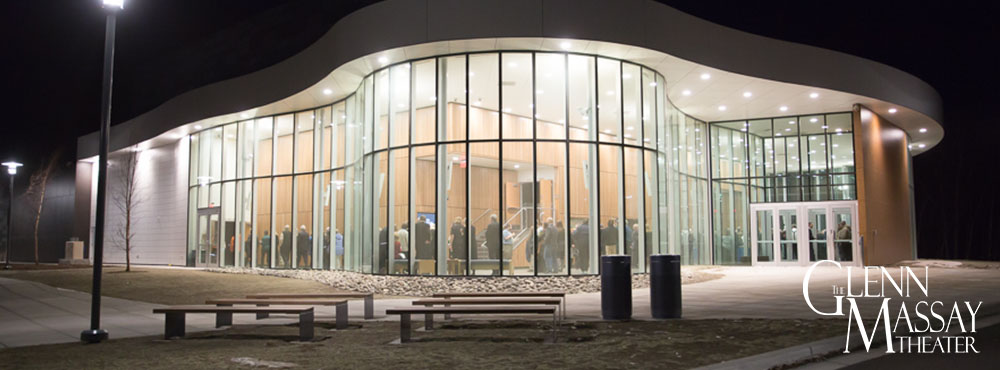 Outside the Glenn Massay Theater at night with the atrium lit up and fill of guests